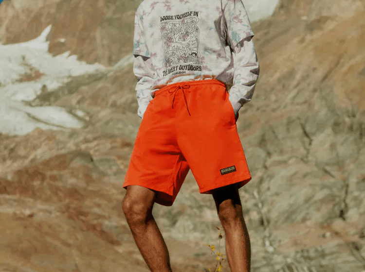 Close-up of bright orange outdoor pants worn in a rocky mountain setting.