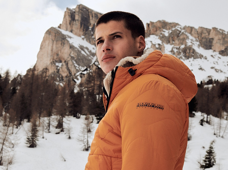 A person wearing orange Napapijri padded jacket in snowy mountain area