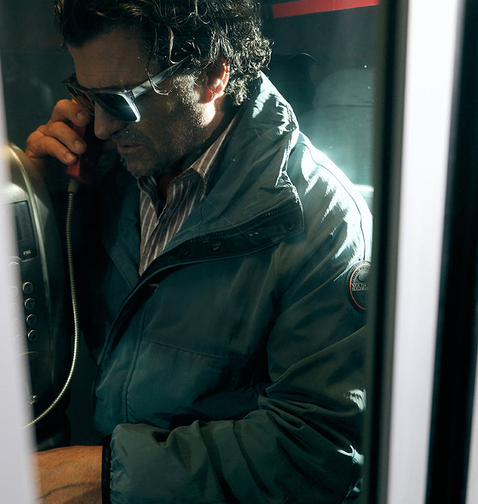 A person wearing blue Napapijri jacket using public telephone indoors