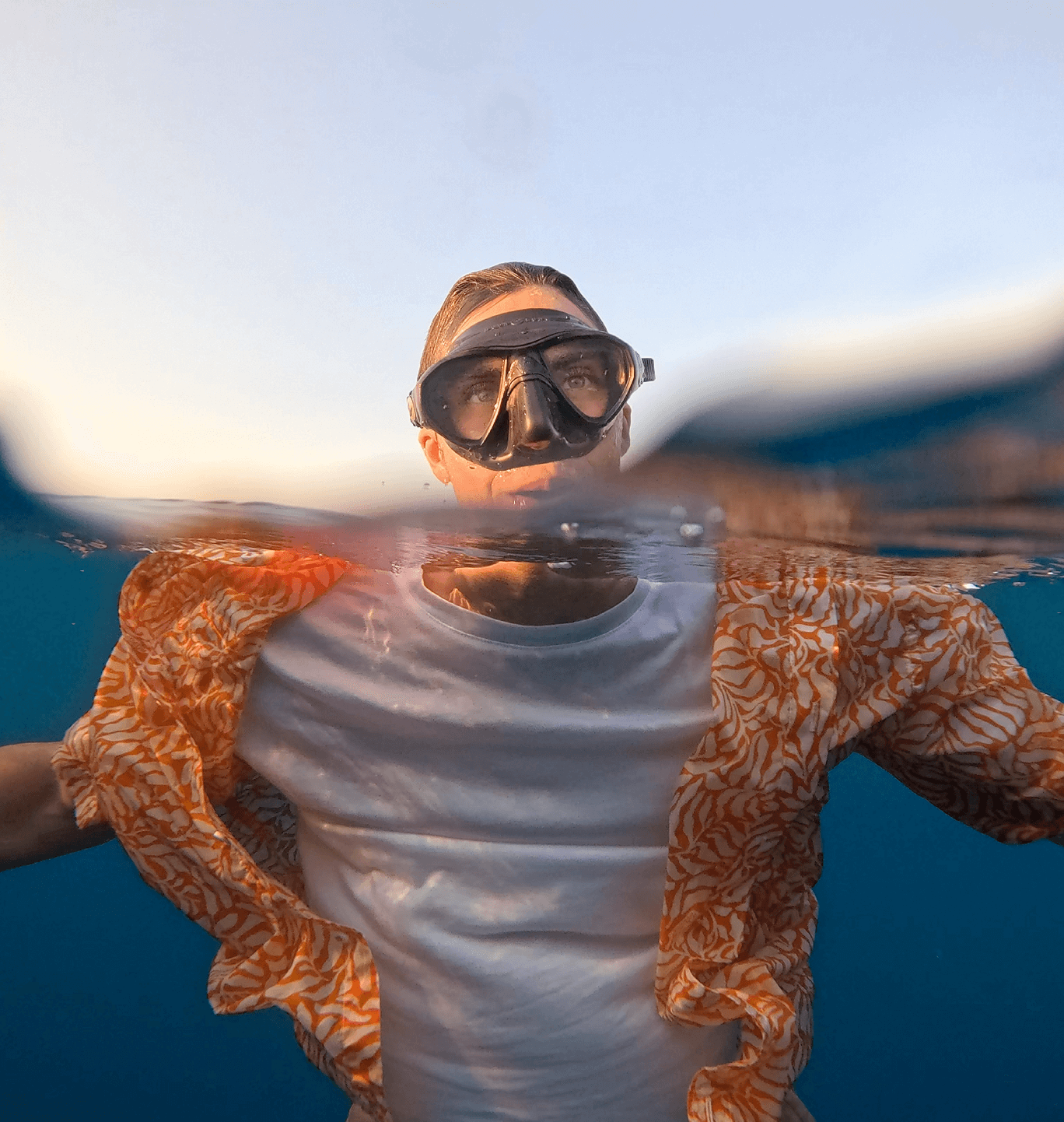 Half-submerged swimmer wearing goggles and patterned shirt at ocean surface