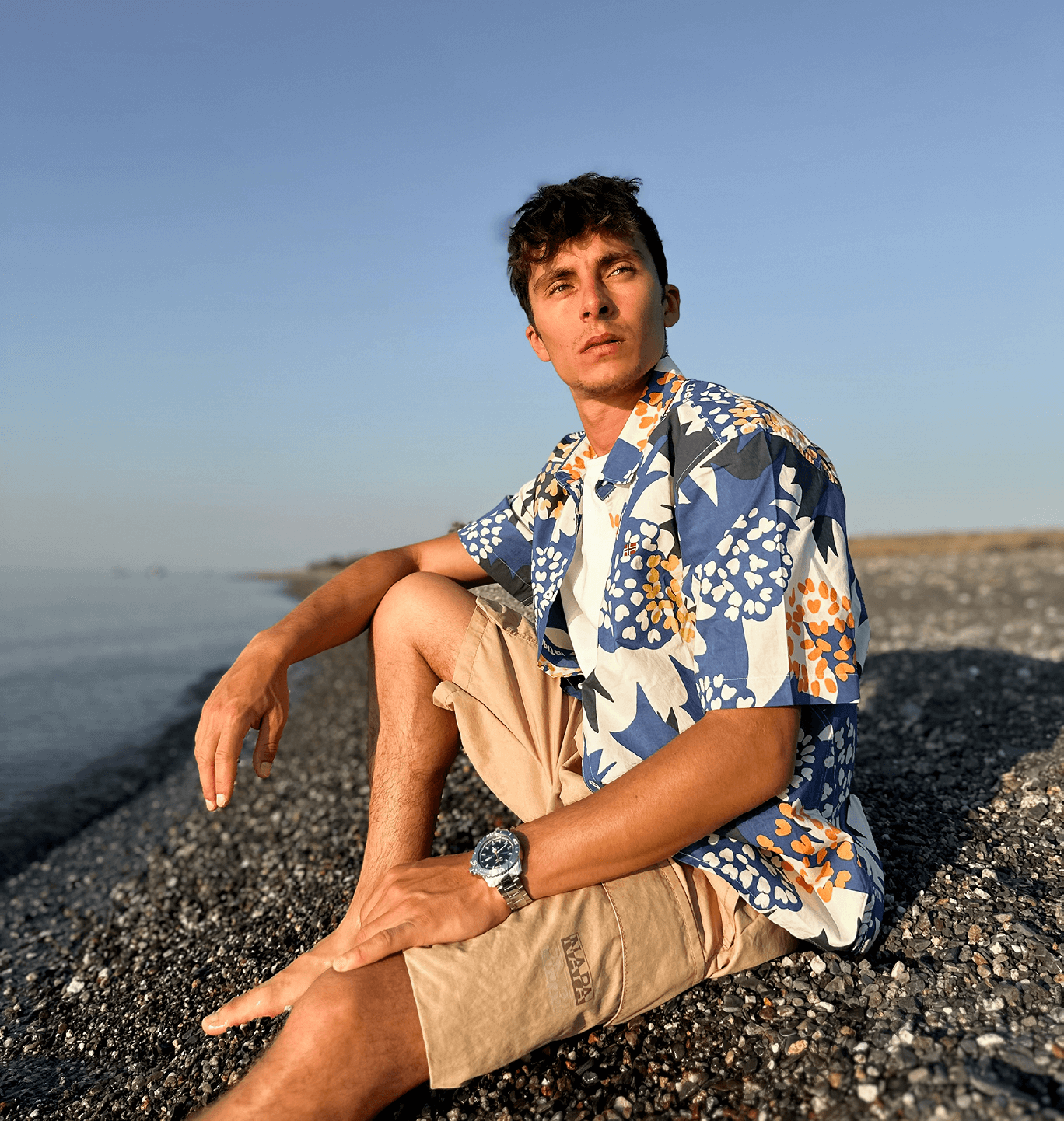 A person wearing short-sleeve patterned shirt and beige shorts on rocky coastline