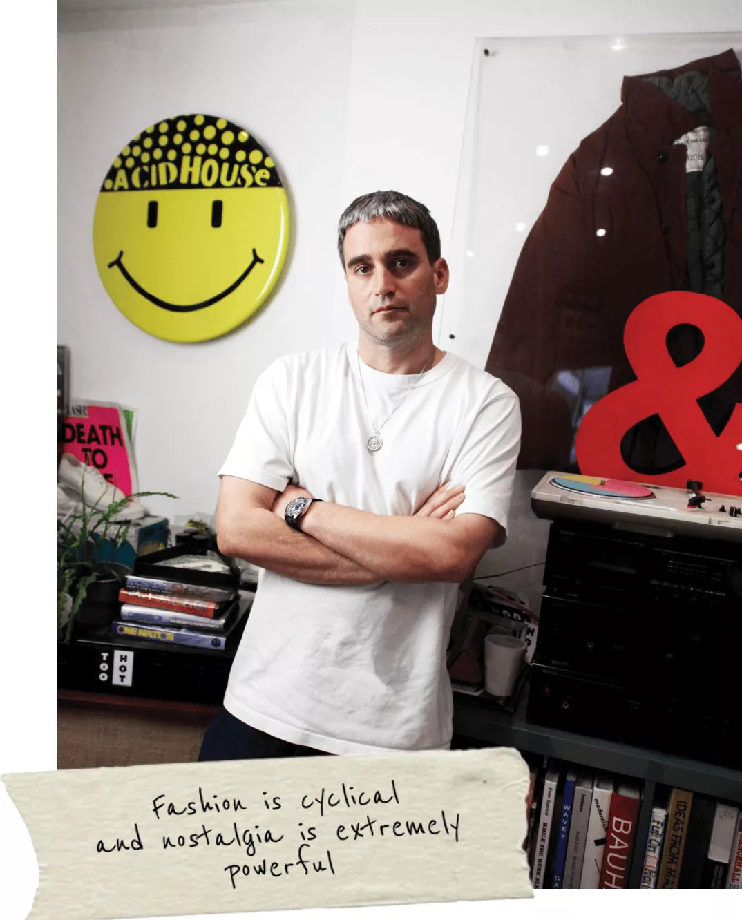 A person standing in studio space with graphic wall art and folded arms.