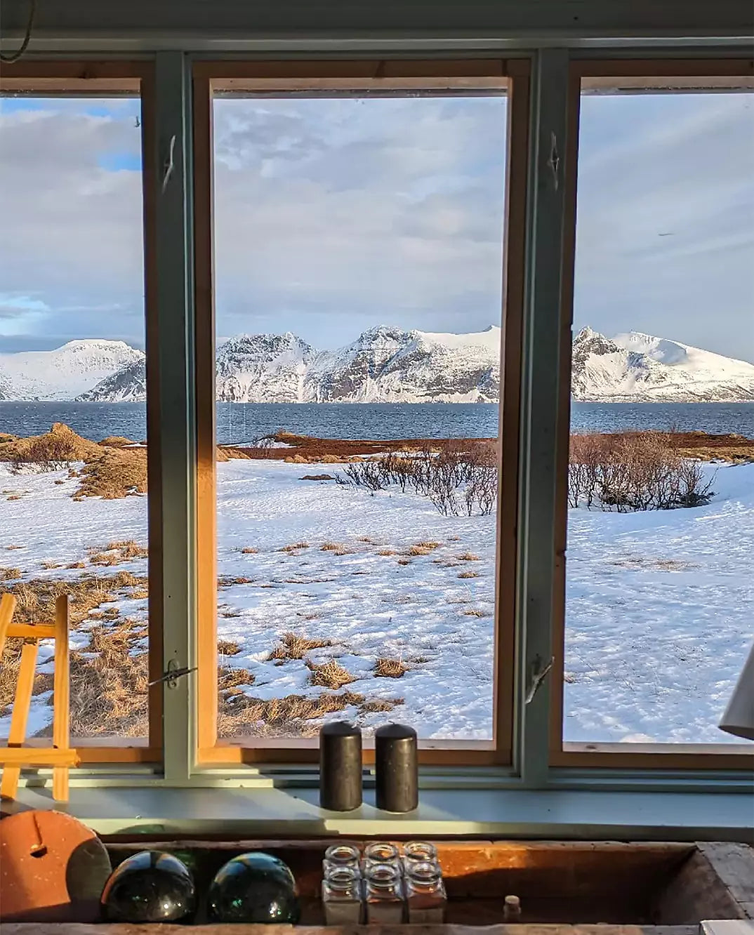 Snow-covered coastal landscape viewed through cabin windows with distant mountains.