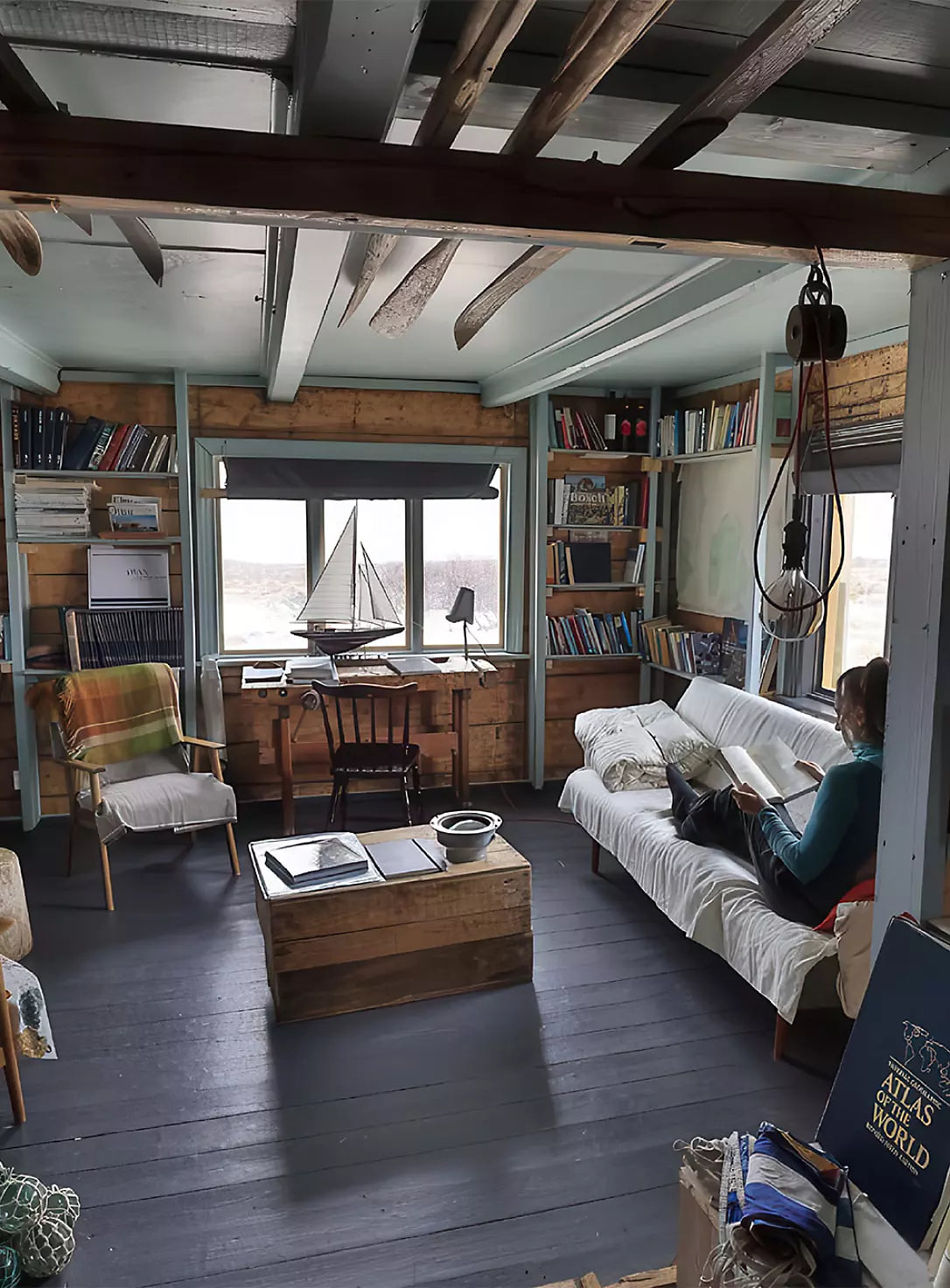 Wooden cabin interior with bookshelves, desk, and sailboat model by window.