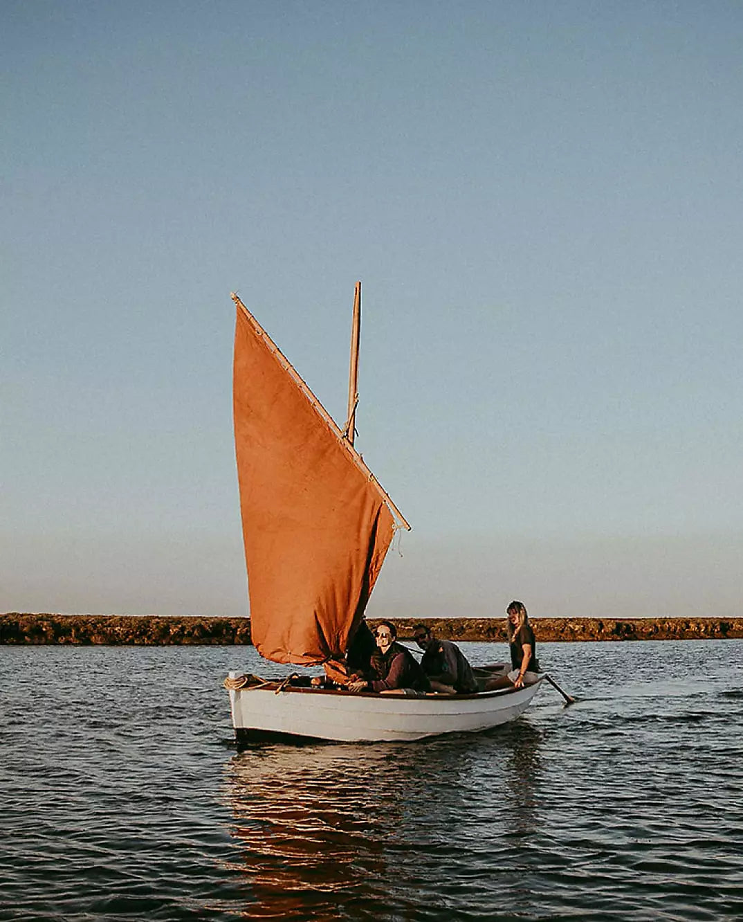 Small sailing boat with brown sail navigating calm coastal waters.