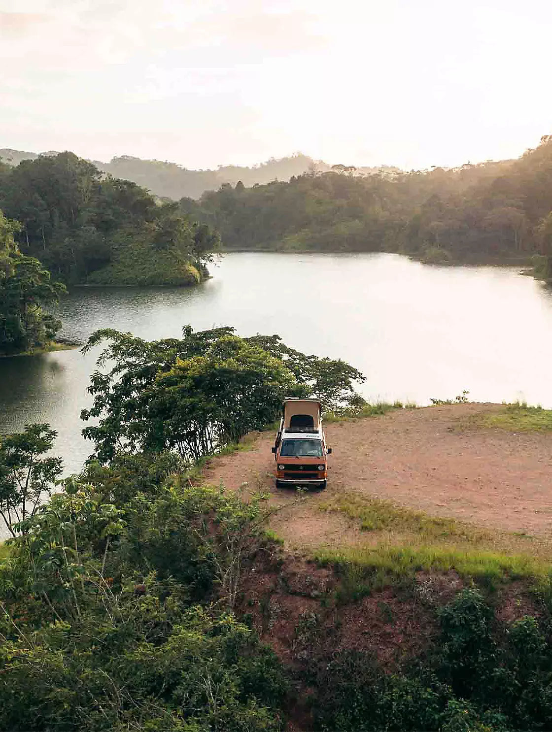Camper van parked beside lake surrounded by forested hills