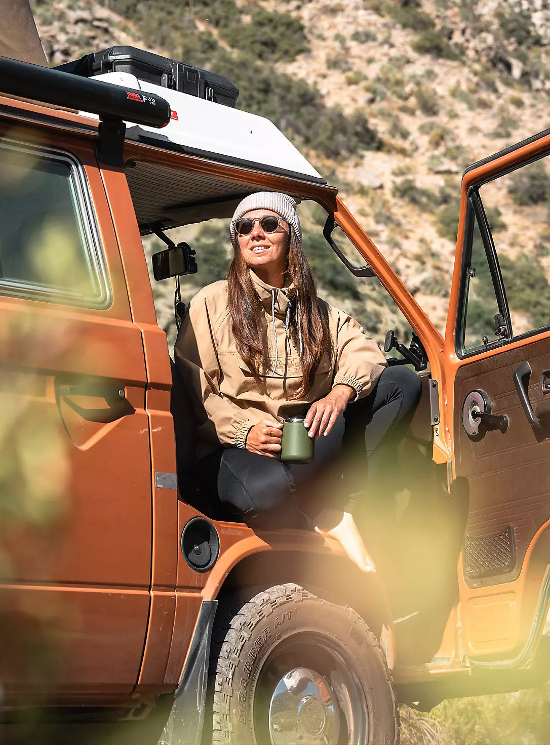 A person wearing a Napapijri jacket sits in a camper van with a drink