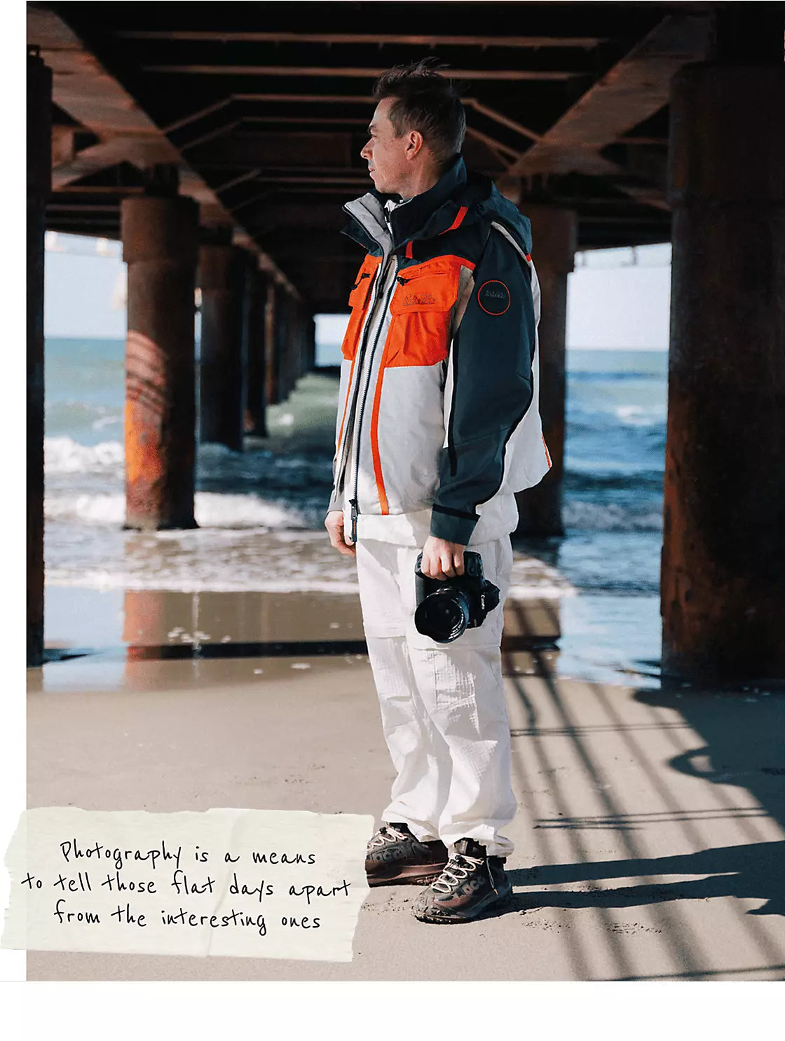 A person wearing Napapijri colour-block jacket near ocean under pier structure